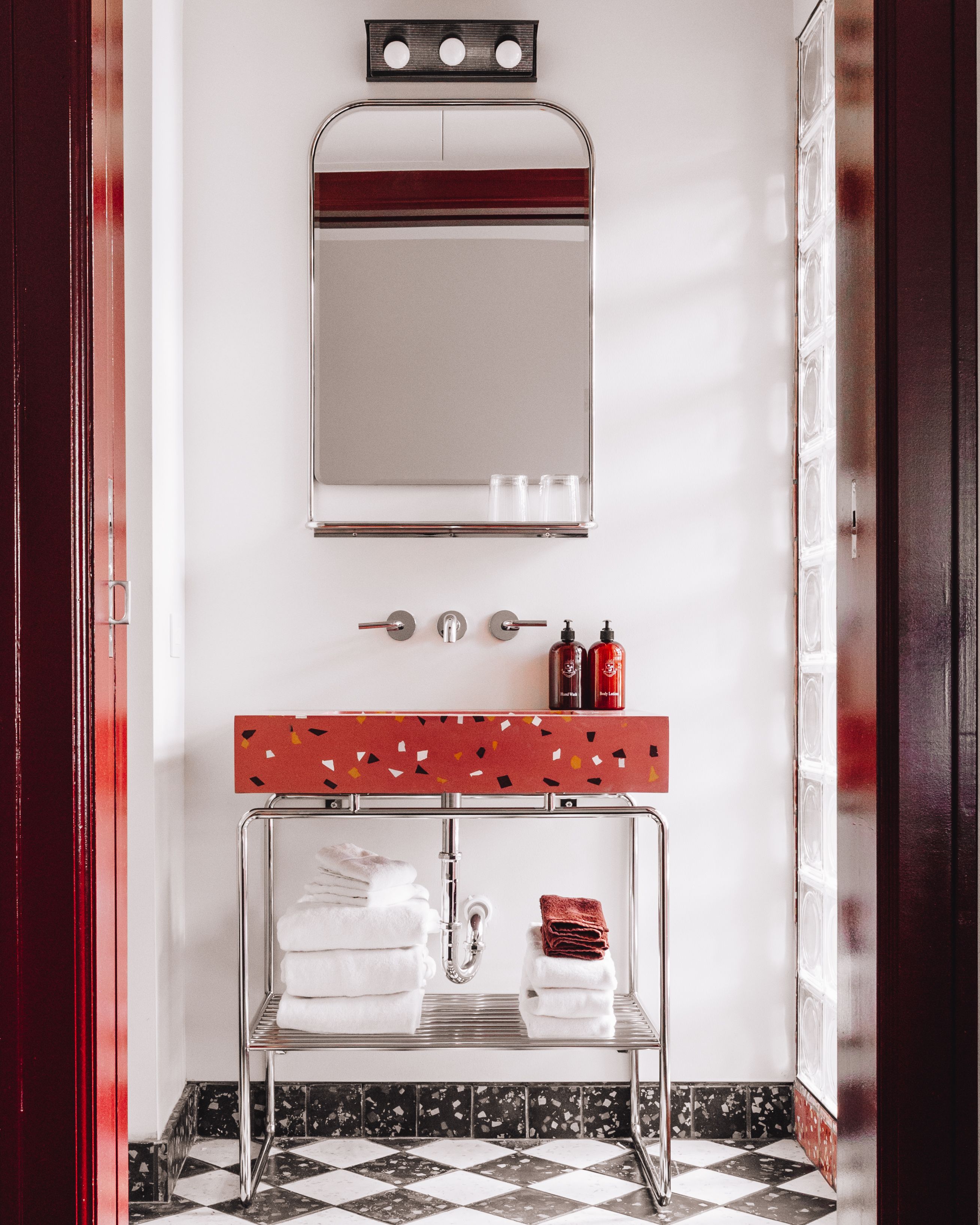 A bathroom with a mirror, a sink with soap dispensers, and a towel rack with folded towels.