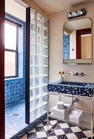 Une salle de bain avec un mur recouvert de carreaux bleus, une douche en verre, un lavabo avec un plan de toilette à motifs bleus, un miroir et un porte-serviettes.