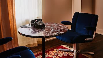 Una habitación con una mesa redonda, dos sillas azules, un tapete floral rojo, un teléfono y un cuadro en la pared.