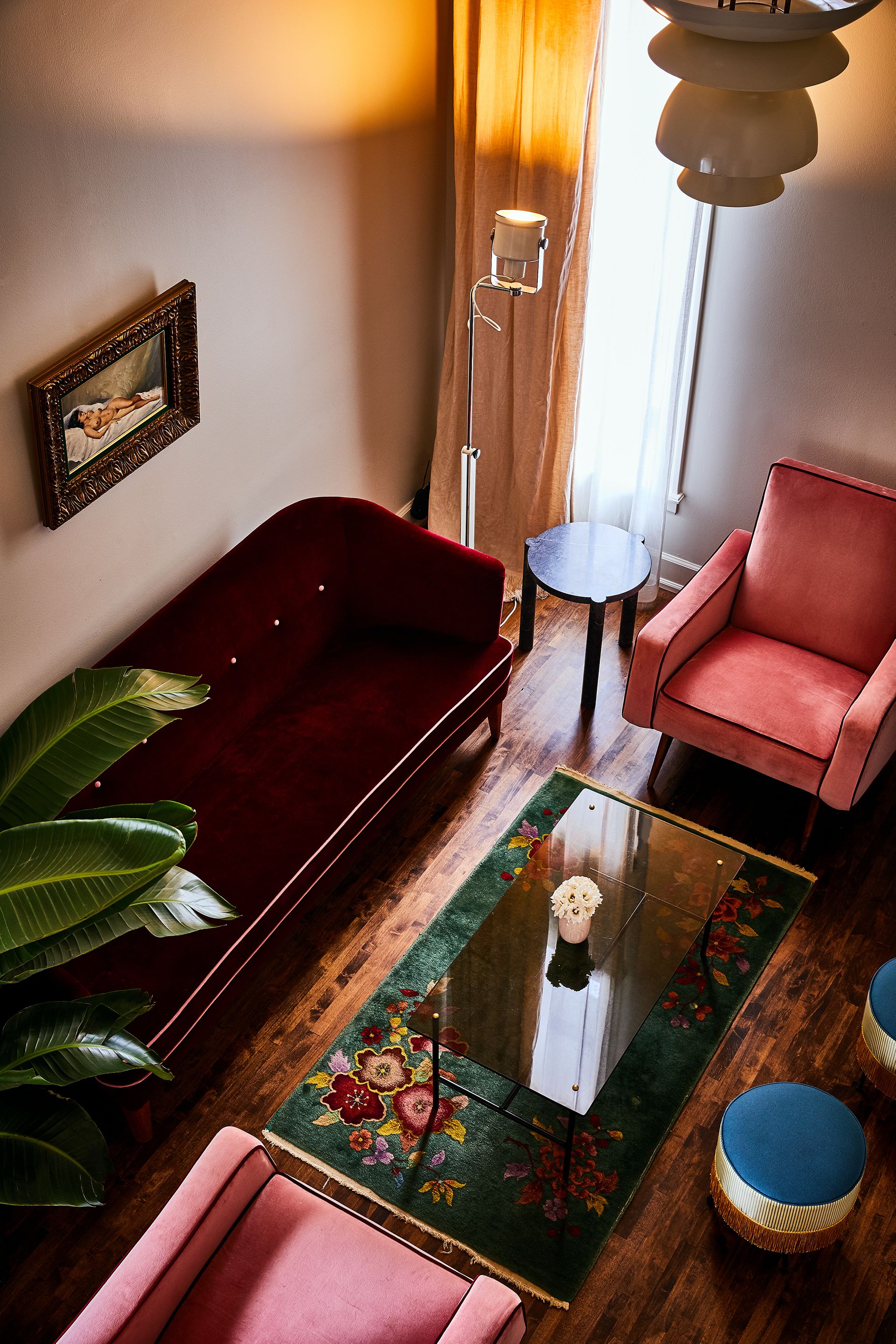 A living room with a red sofa, a pink armchair, a small table with a vase, and a green floral rug.
