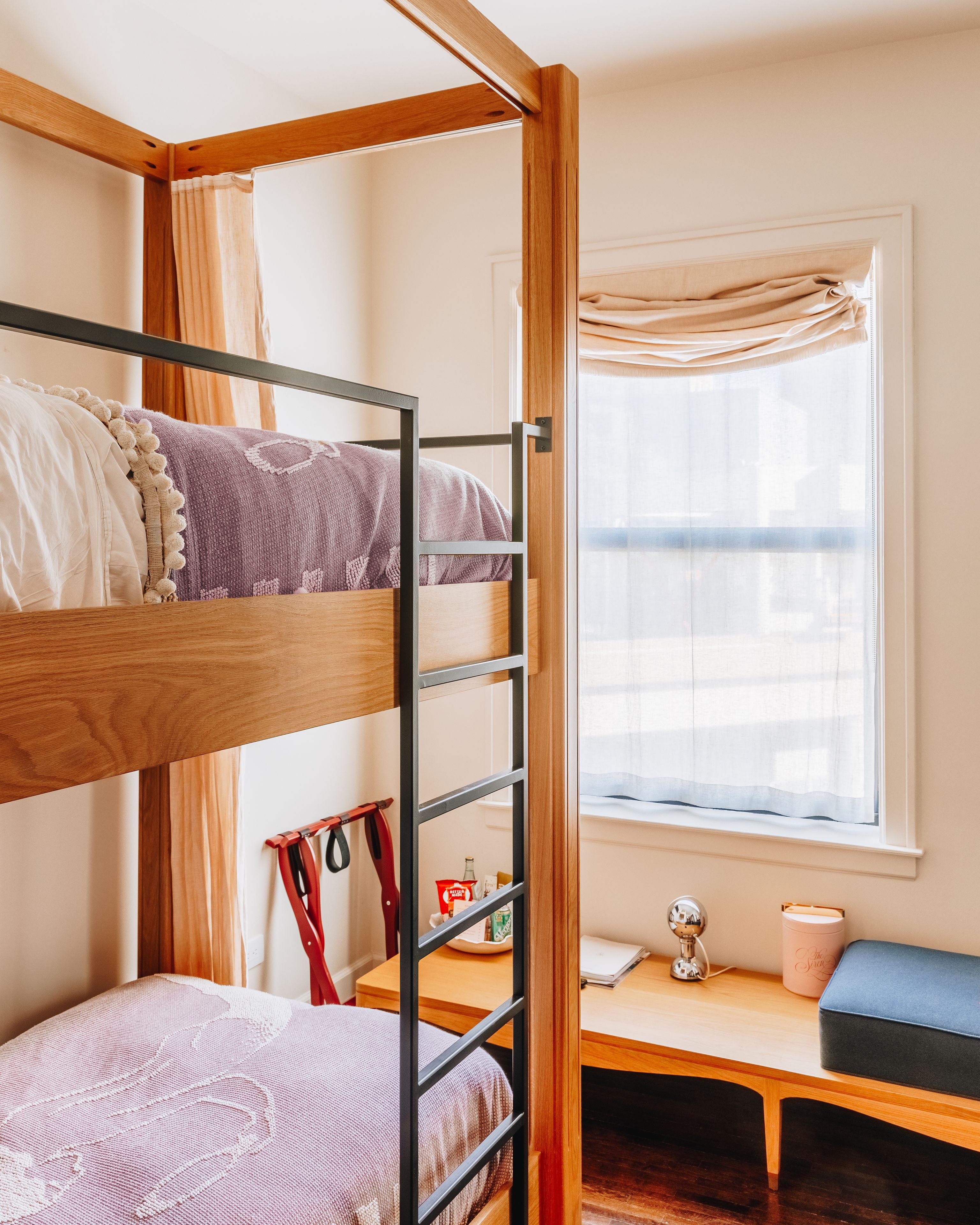 Un lit superposé avec un bureau et une chaise, une fenêtre avec des rideaux et une petite table avec une lampe et une tasse.