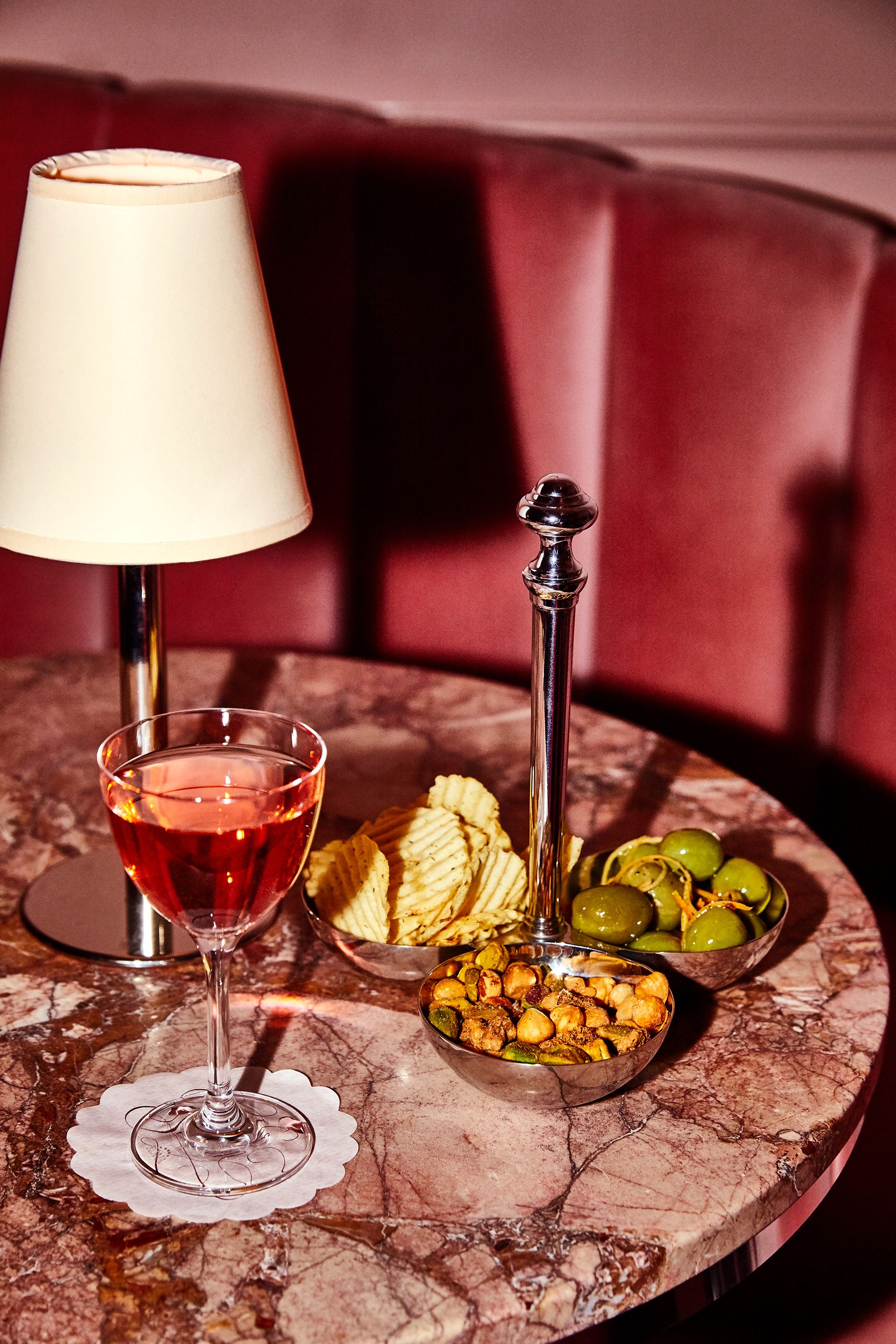 A table with a glass of red wine, a bowl of olives, and a plate of nuts.