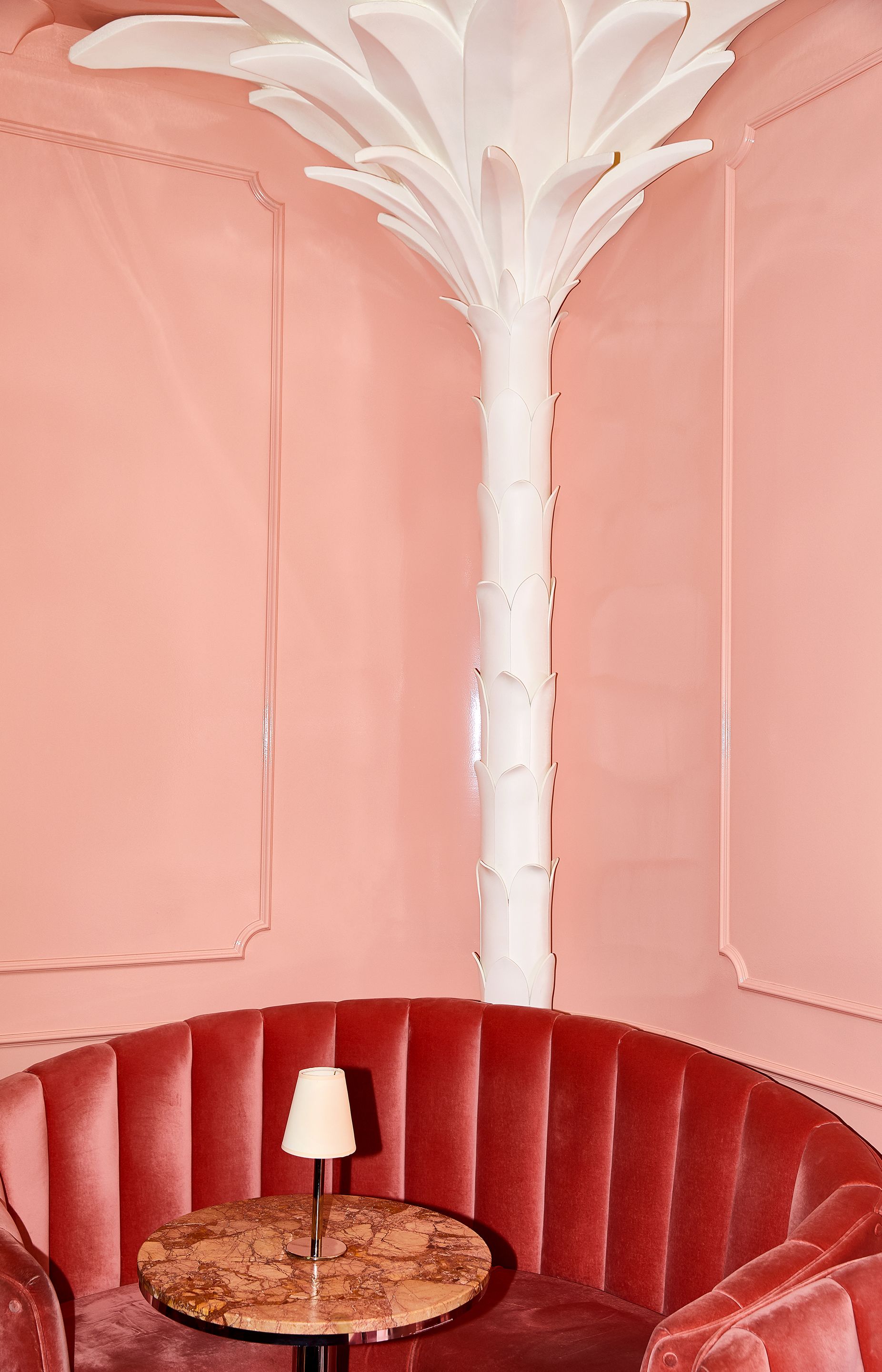 Banca estofada em vermelho com uma mesa de mármore e uma luminária branca.
