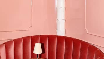 Banca estofada em vermelho com uma mesa de mármore e uma luminária branca.