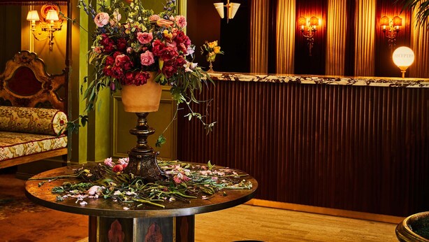 A lobby with a chandelier, a reception desk, a sofa, and a table with flowers. - The Siren Hotel, an Ash Hotel (Detroit)