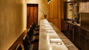 A long dining table with chairs, a kitchen area, and pendant lighting. - The Siren Hotel, an Ash Hotel (Detroit)