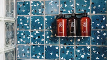 A bathroom with blue mosaic tiles and three bottles of shampoo, body wash, and conditioner.