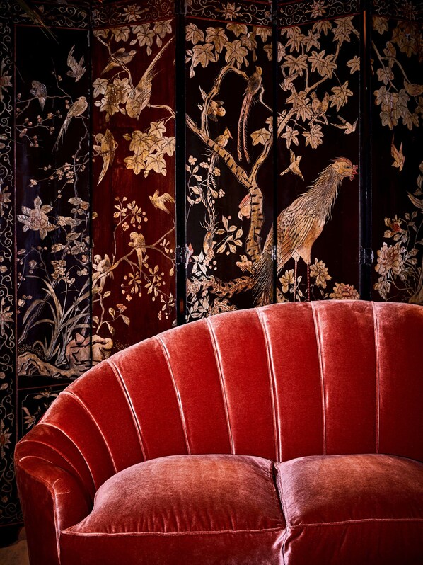 Un sofá de terciopelo rojo frente a un panel decorativo con diseños intrincados de aves y flores.