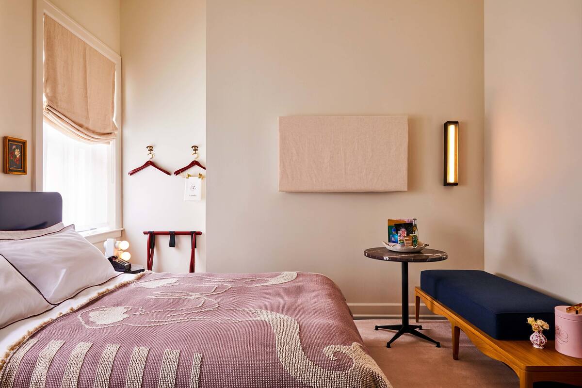 A bedroom with a bed, bedside table, bench, and a wall-mounted light fixture.