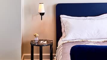 Un dormitorio ordenado con una cama, una mesita de noche con lámpara y una pequeña mesa redonda con un florero.