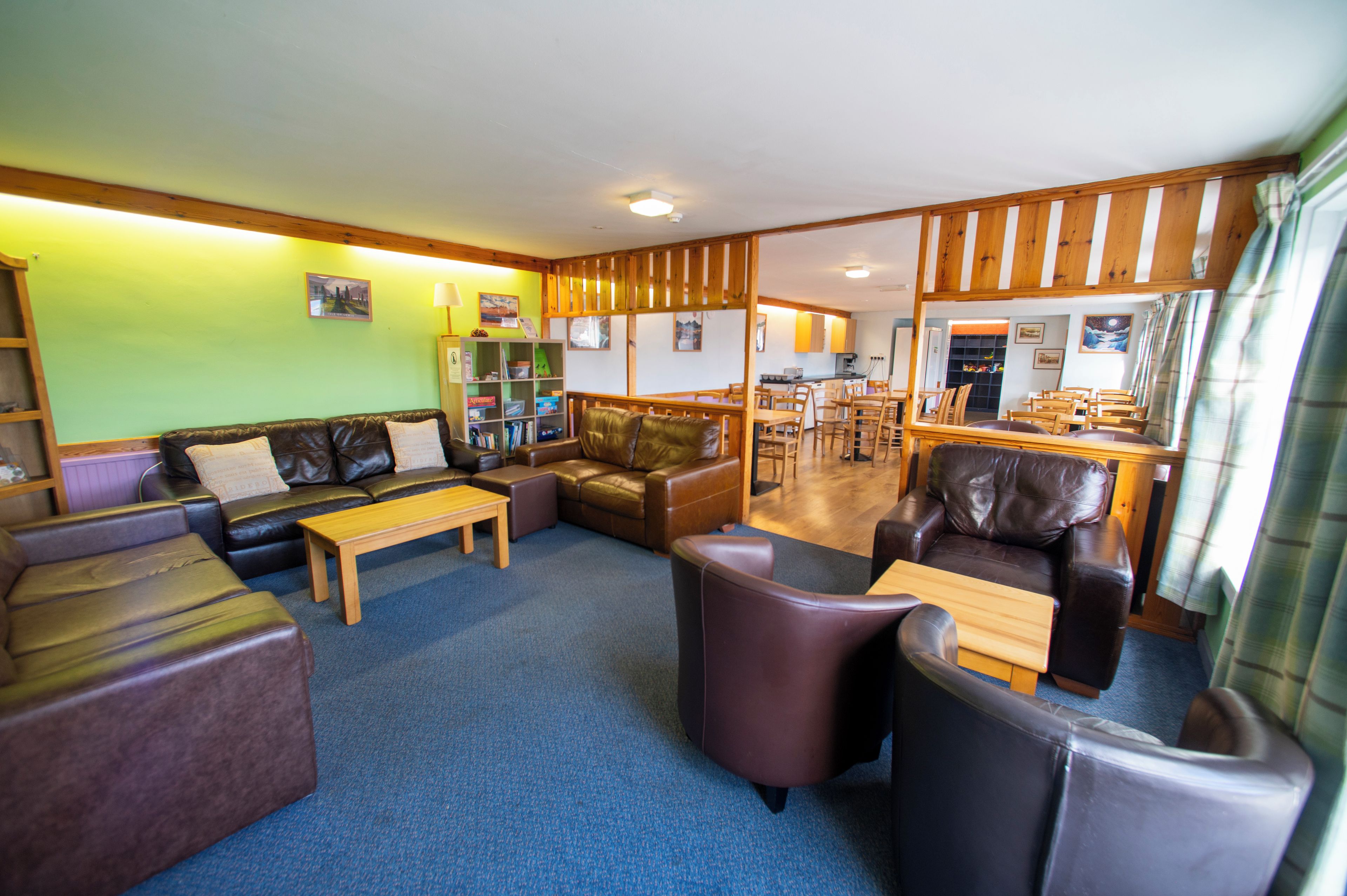 A hotel lobby with leather sofas, a wooden coffee table, and a dining area with wooden chairs and tables.