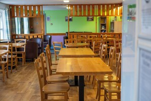 Un espace repas comprenant plusieurs tables et chaises en bois, un mur vert orné d’œuvres d’art et une cloison en bois.