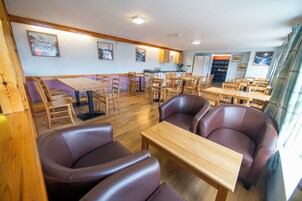 Un comedor con mesas y sillas de madera, una cocina al fondo y obras de arte en las paredes.