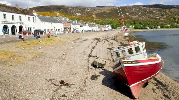 A coastal town with a row of white buildings, a red boat named 'Northern Lights' docked on the shore, and a clear sky. - Ullapool Youth Hostel (Ullapool)