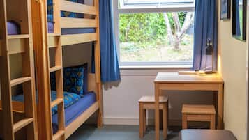 A bunk bed room with a desk and chair, a window with curtains, and a view of greenery outside.