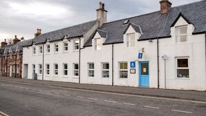 A row of white buildings with grey roofs, a blue door, and a sign indicating a hotel. - Ullapool Youth Hostel (Ullapool)