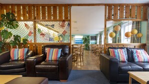 A cozy lobby with leather sofas, wooden tables, and a netted partition with colorful artwork. - Ullapool Youth Hostel (Ullapool)