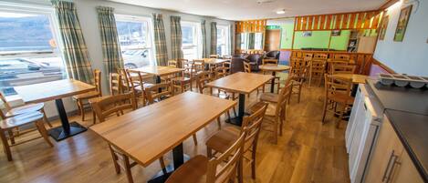 A restaurant with wooden tables and chairs, large windows with curtains, and a view of the outside.