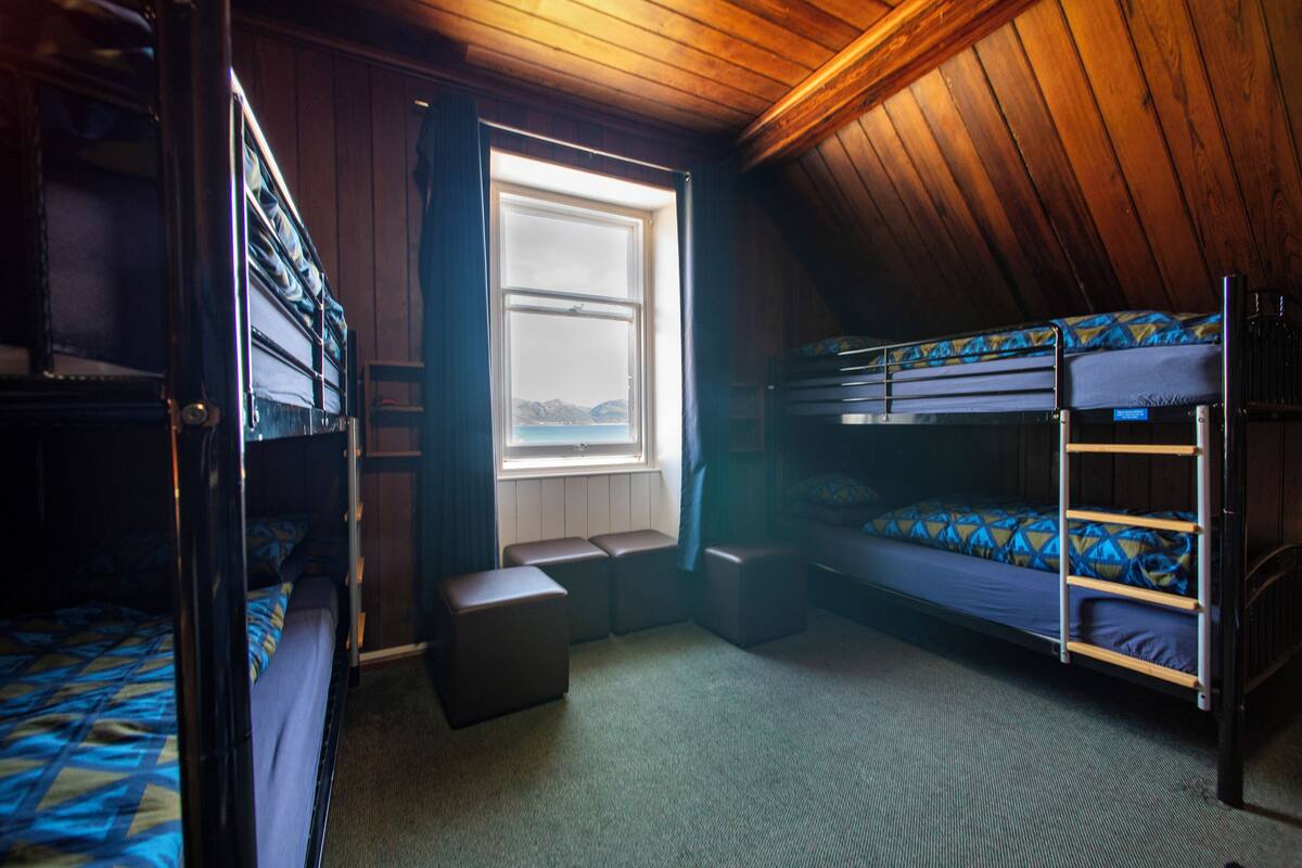 A dormitory room with bunk beds, a window, and a wooden ceiling.