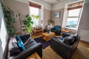 Ein Wohnzimmer mit einer Couch, einem Couchtisch und einer TV-Bank. Pflanzen und ein Fenster mit Blick.