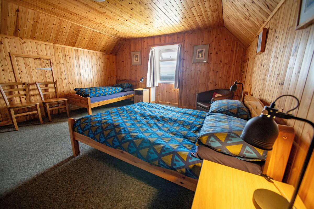 A wooden cabin bedroom with two beds, a desk, and a chair.