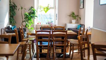 A dining area with wooden tables and chairs, a sofa, and potted plants.