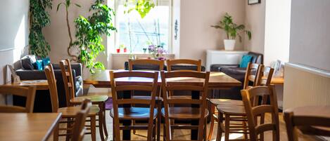 A dining area with wooden tables and chairs, a sofa, and potted plants.
