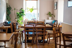 Un área de comedor con mesas y sillas de madera, un sofá y plantas en macetas.