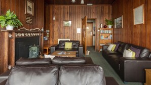Una habitación con paneles de madera, sofás de cuero, una chimenea, una estantería y una puerta que da a otra habitación.