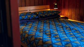 Een bed met een deken en kussens met een geometrisch patroon, een houten hoofdbord en een bedlampje.