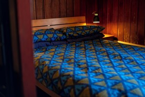 A bed with a geometric patterned bedspread and pillows, a wooden headboard, and a bedside lamp. - Gairloch Sands Youth Hostel (Gairloch)
