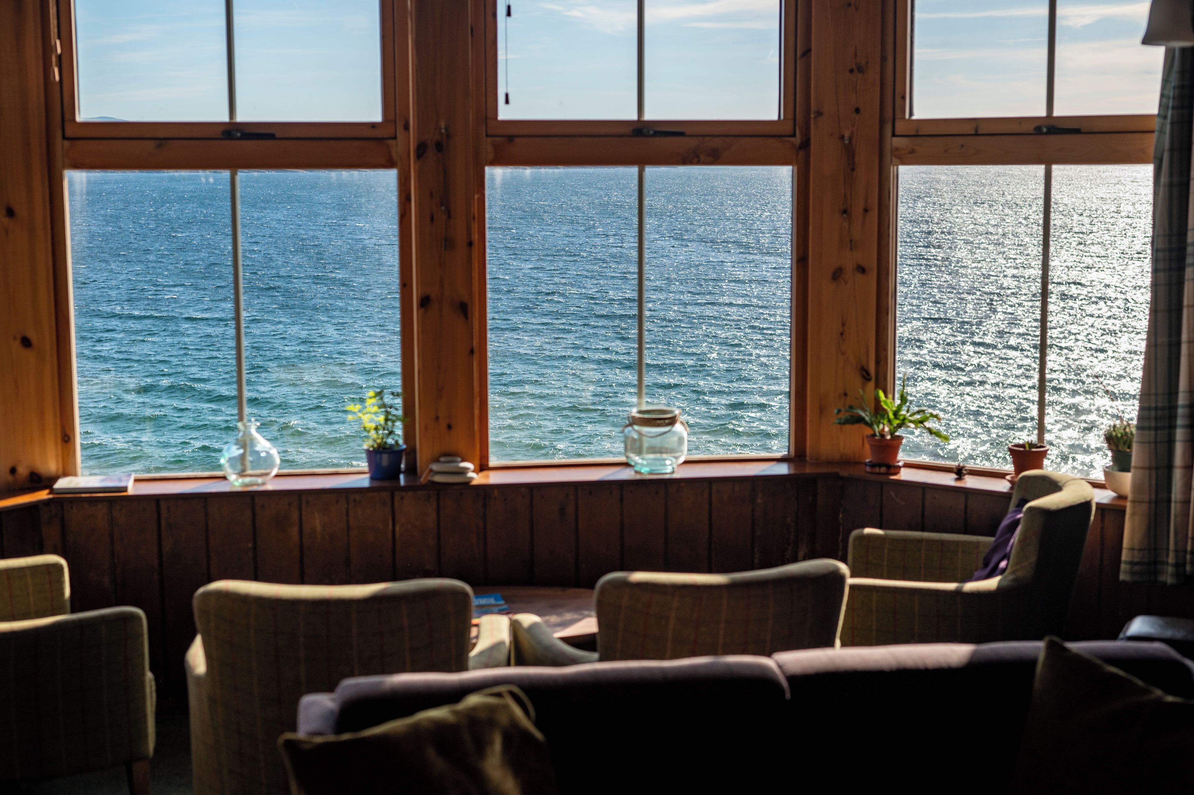 Ein Zimmer mit Meerblick durch große Fenster, mit Holzwänden und mehreren Stühlen.