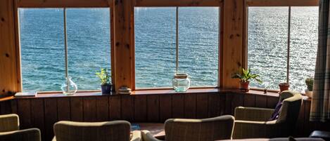 Ein Zimmer mit Meerblick durch große Fenster, mit Holzwänden und mehreren Stühlen.