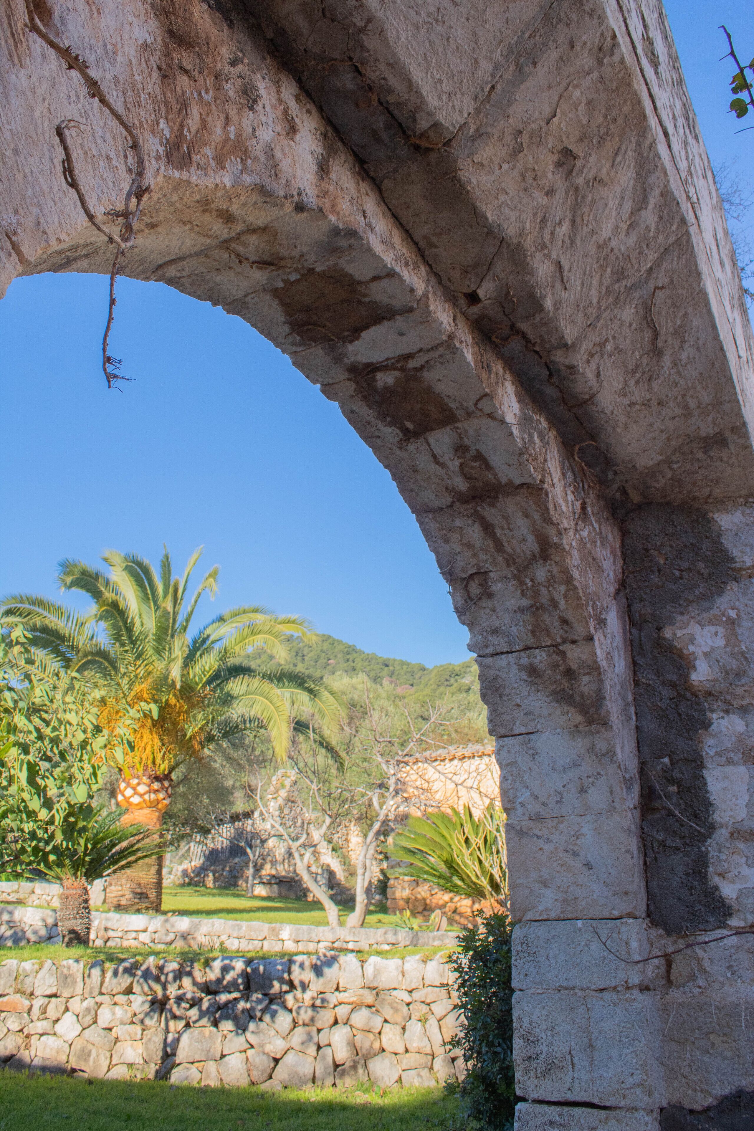 En gammal stenvalvbåge med utsikt över en frodig trädgård och en kulle i bakgrunden.