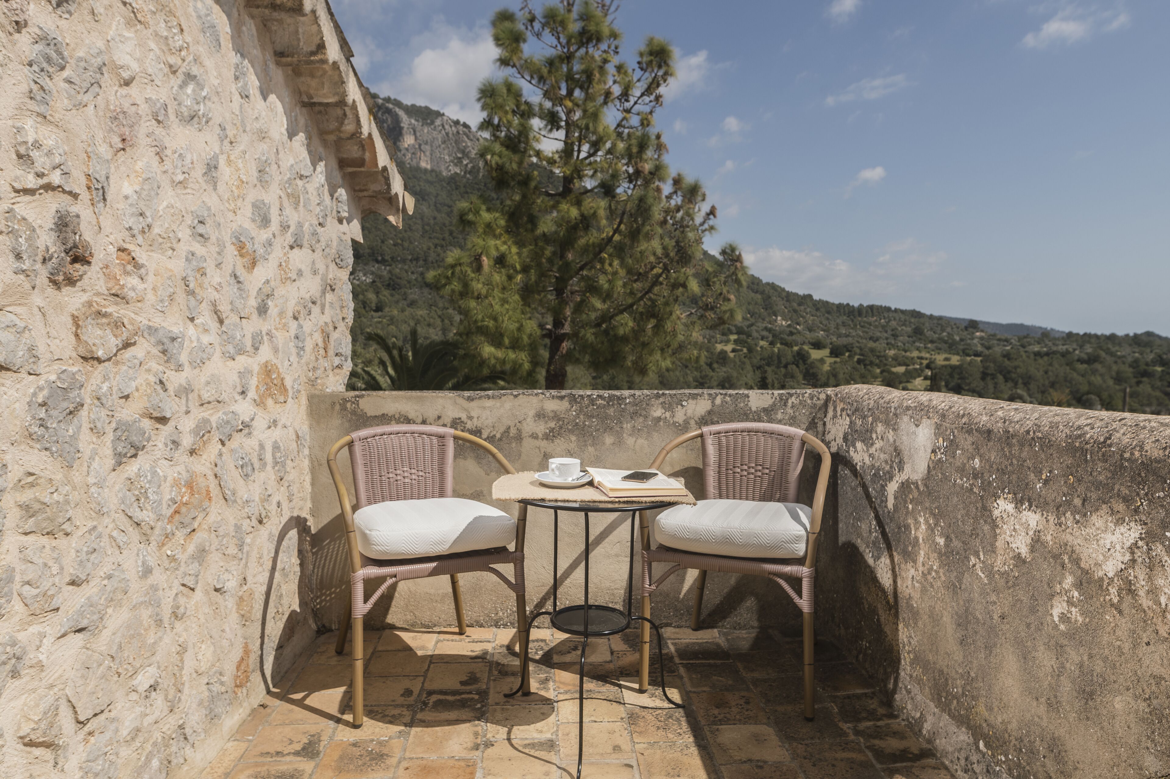 Una terraza con dos sillas de mimbre y una mesita, con vistas a un paisaje montañoso.