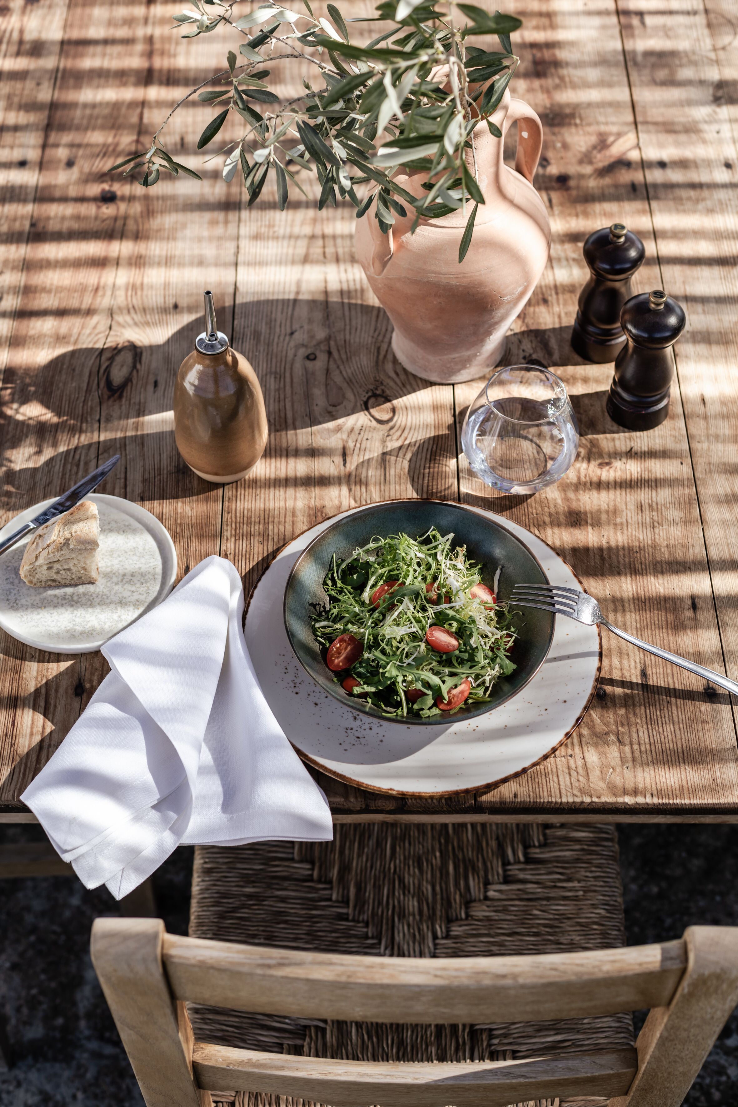 Una mesa de madera con una ensalada en un plato, una jarrón, un vaso de agua y un salero.