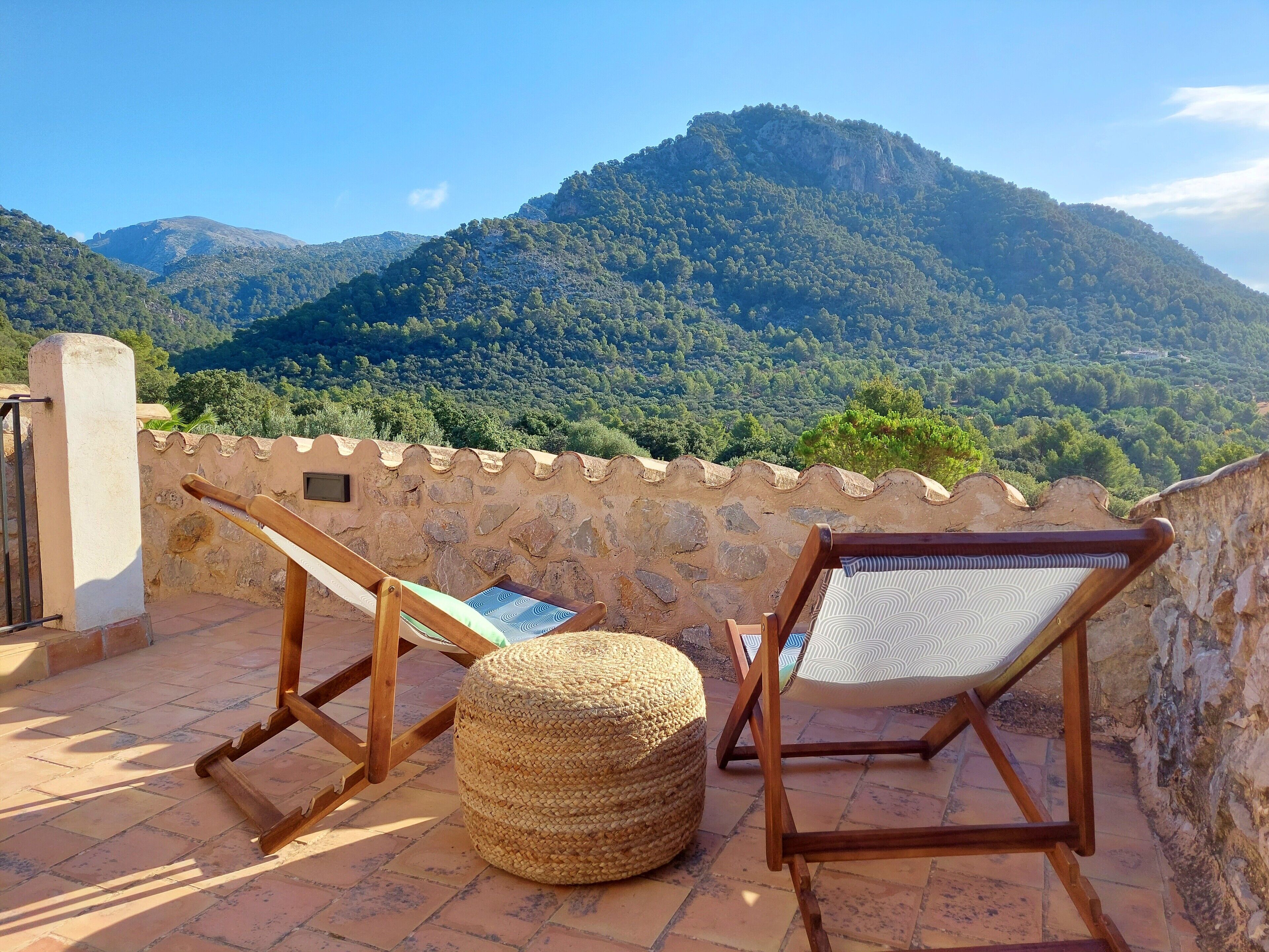 Una terraza con dos sillas de madera y un reposapiés tejido, con vistas a un paisaje montañoso.