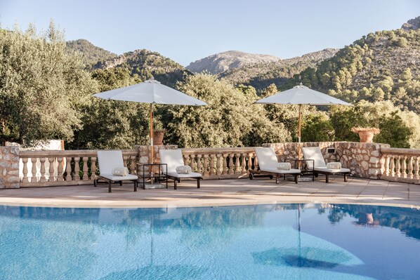 A poolside area with lounge chairs and umbrellas, set against a mountainous backdrop. -  Finca Can Beneït (Selva)