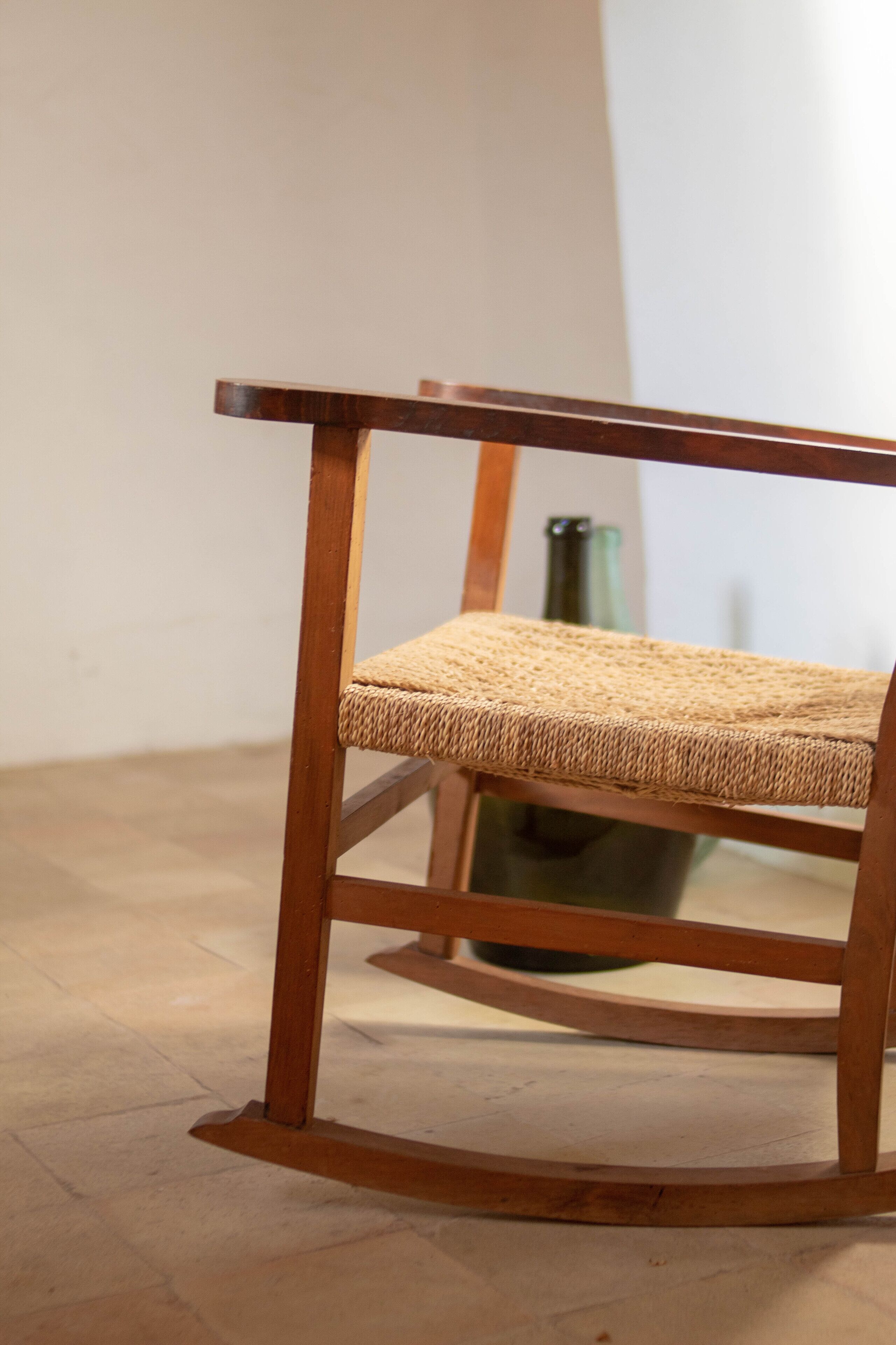 Una silla de madera con asiento y respaldo trenzado, sobre un suelo de baldosas.
