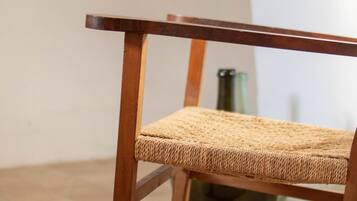 Una silla de madera con asiento y respaldo trenzado, sobre un suelo de baldosas.