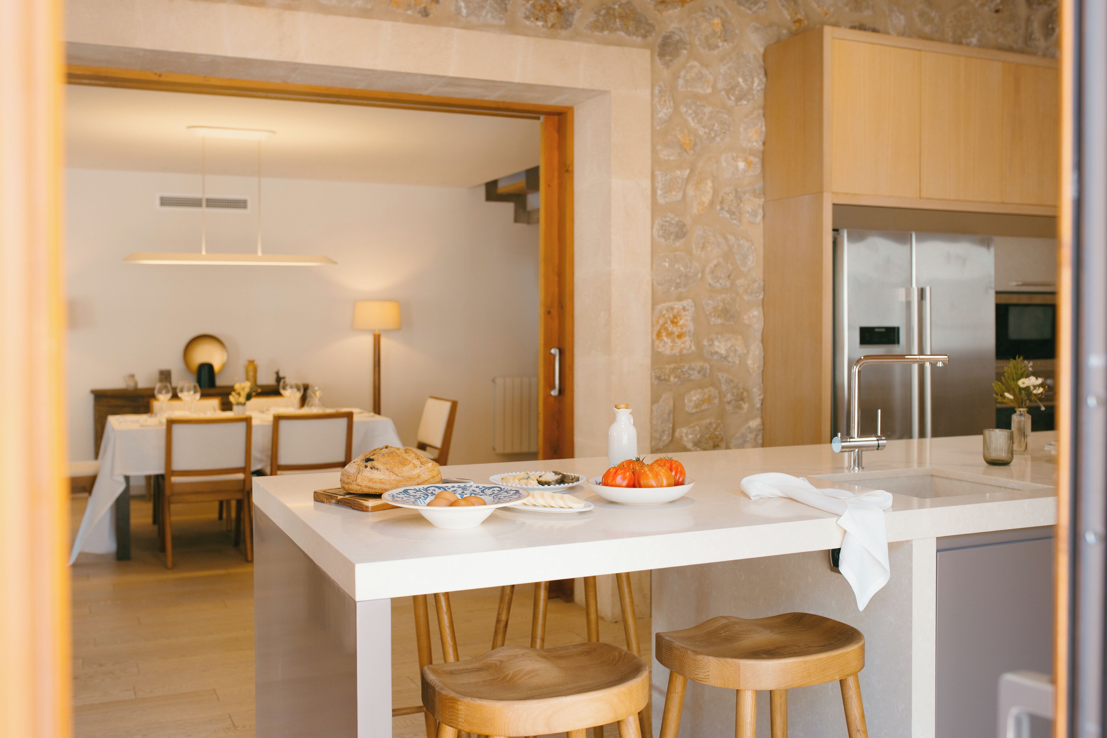 Una cocina moderna con una isla central, taburetes de madera y un comedor al fondo.