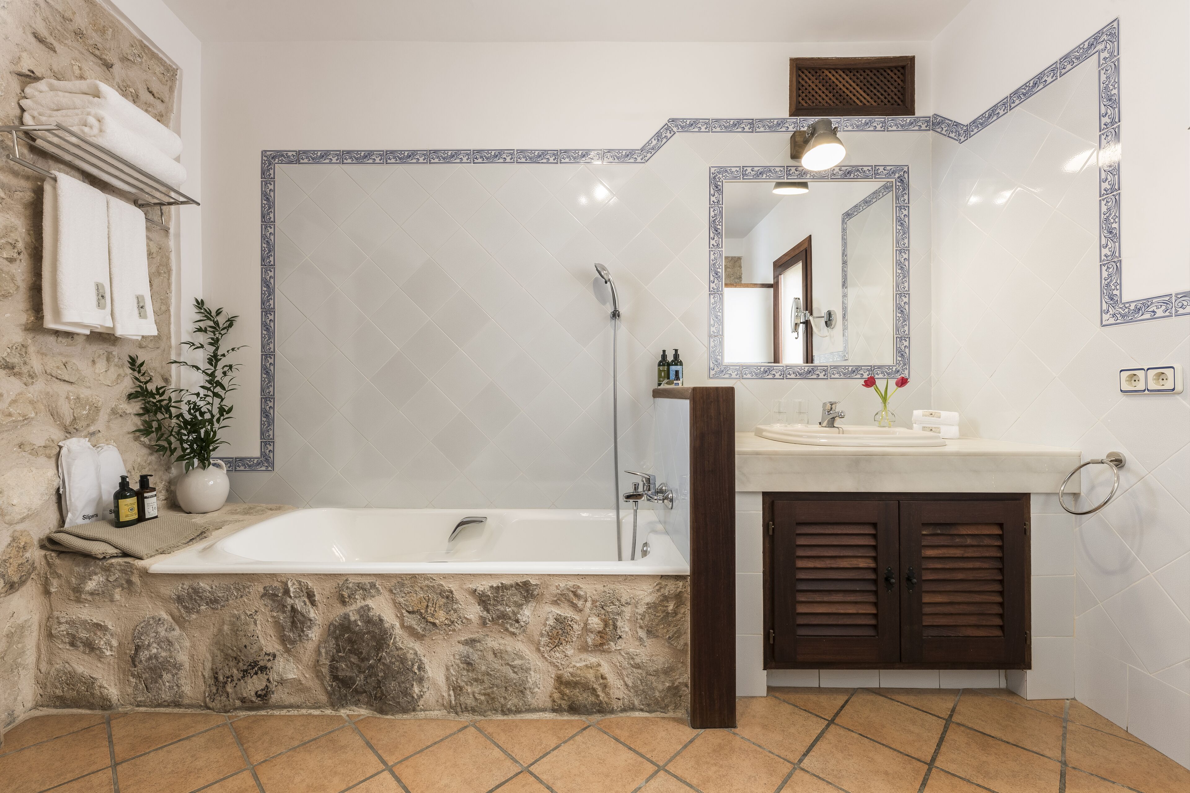 Une salle de bain avec un mur en pierre, une baignoire, un lavabo et un miroir.