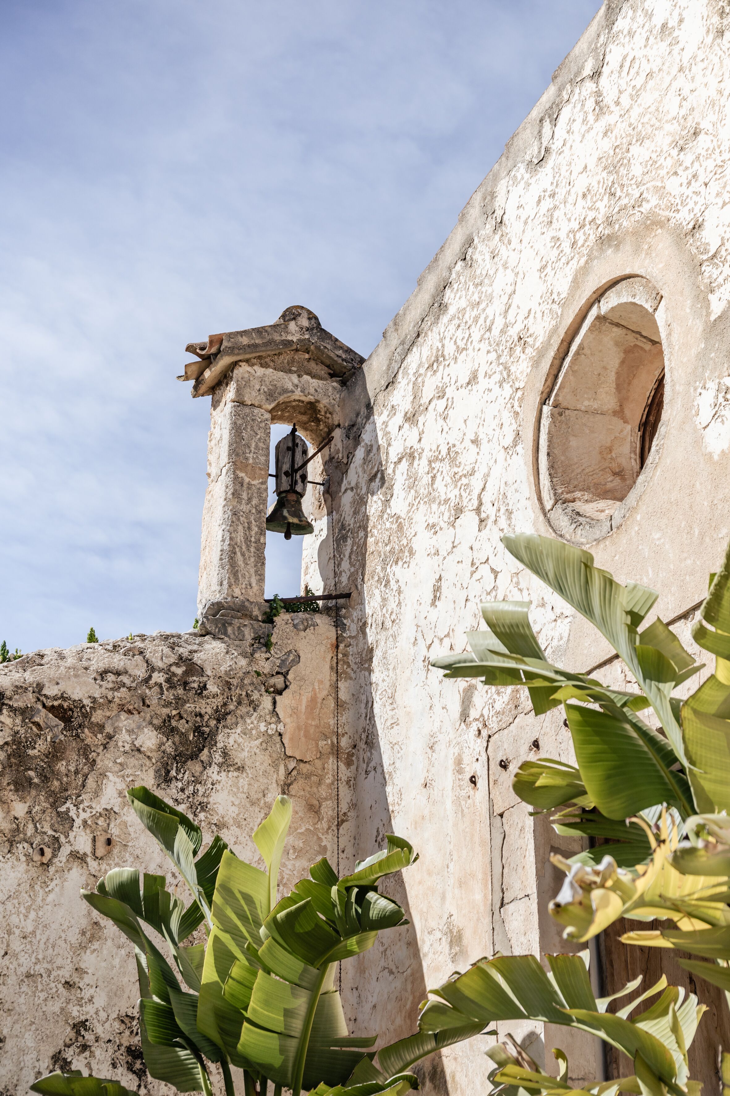 A weathered building with a bell tower and a circular window.