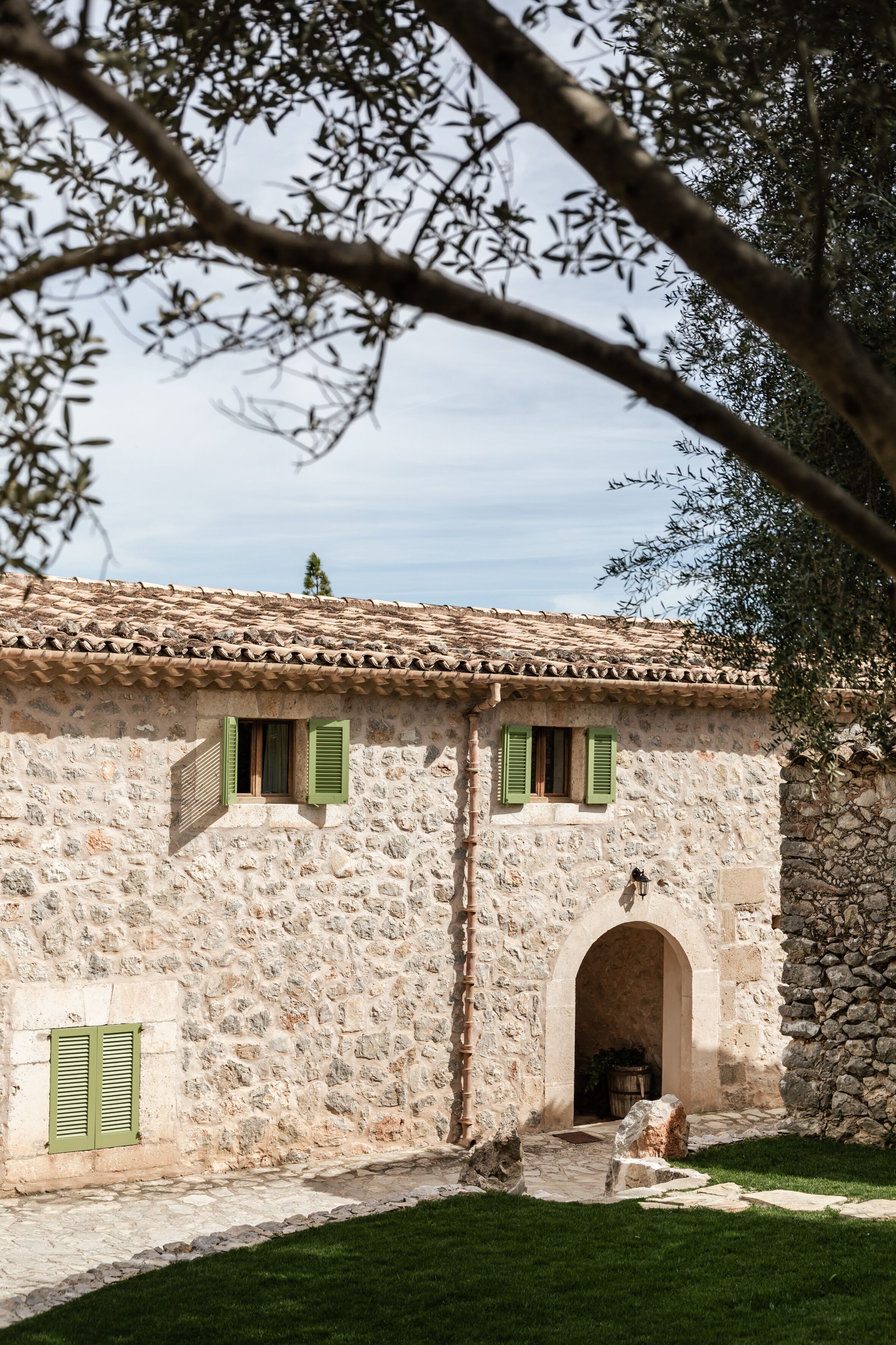 Edificio de piedra con techo de tejas, contraventanas verdes y un arco de piedra que conduce a la entrada.