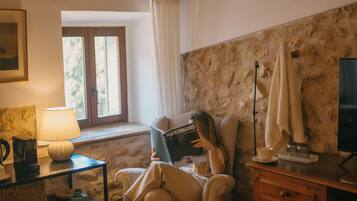 Una habitación acogedora con techo de madera, una ventana con cortinas, una lámpara, un sofá, un televisor y una estantería.