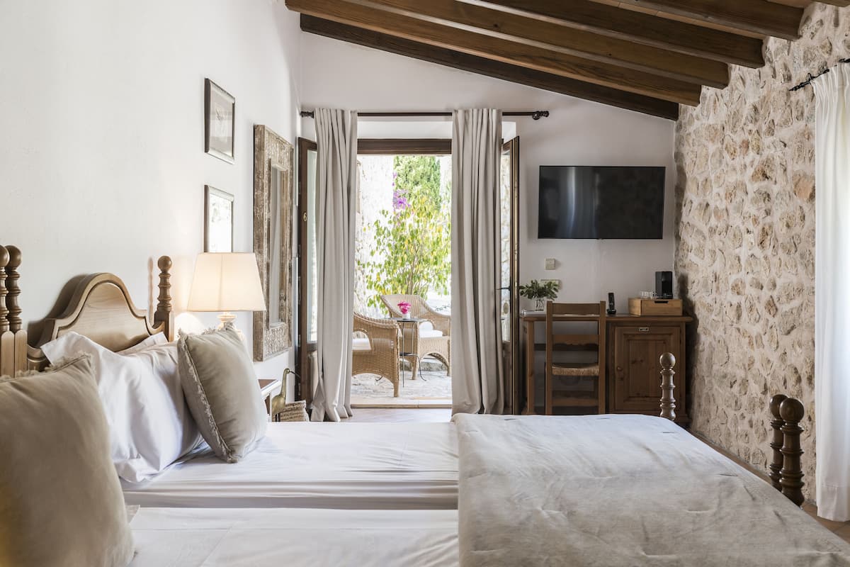 A bedroom with a bed, a desk, and a TV. There is a window with curtains and a view of the outside.