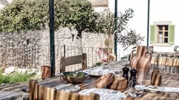 Mesa de comedor al aire libre con sillas de madera, un tazón de ensalada y diferentes utensilios de mesa.