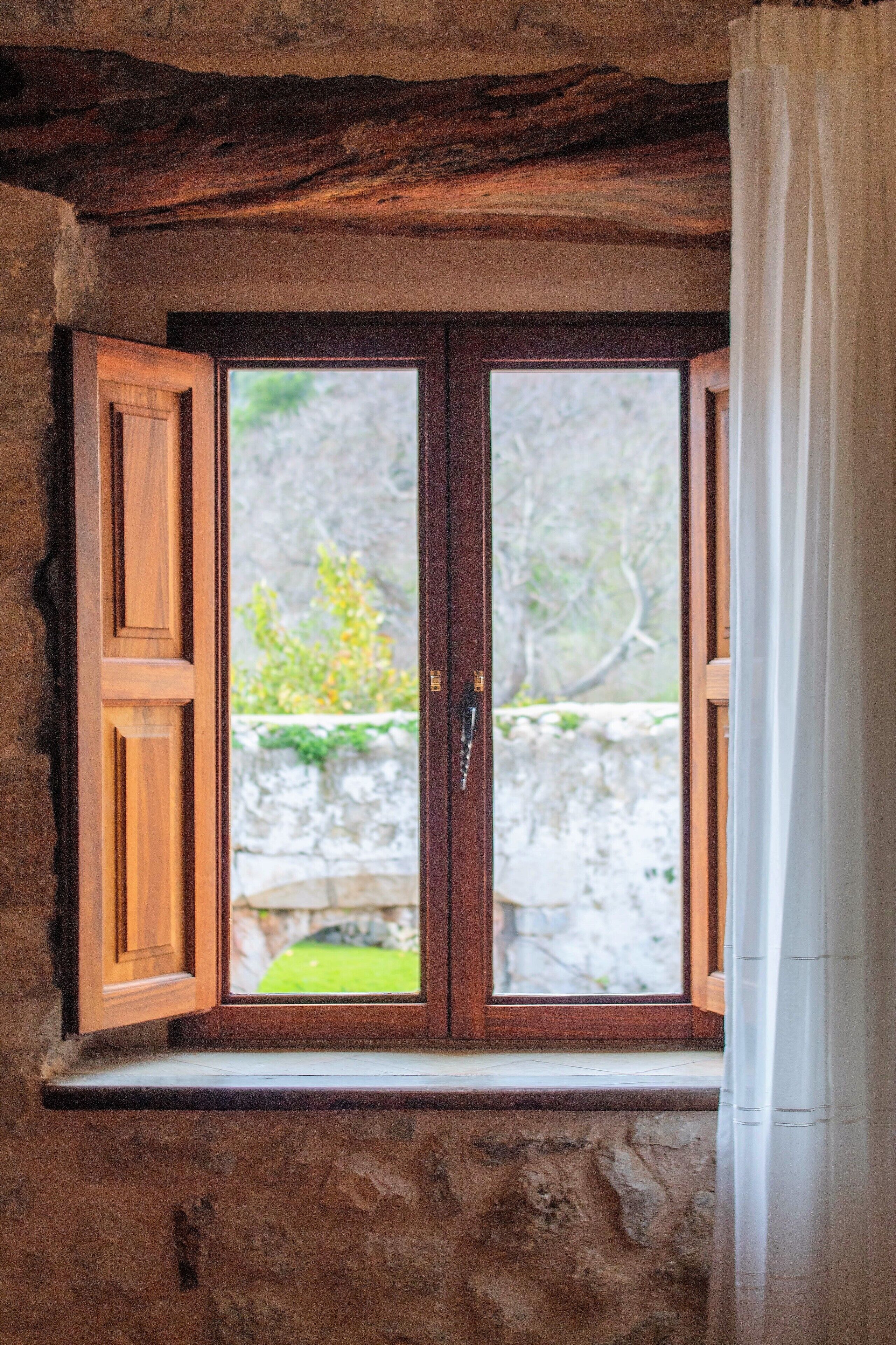A wooden-framed window with a stone wall and a view of greenery outside.