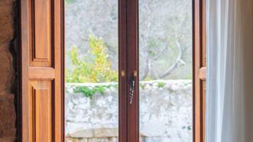 A wooden-framed window with a stone wall and a view of greenery outside.