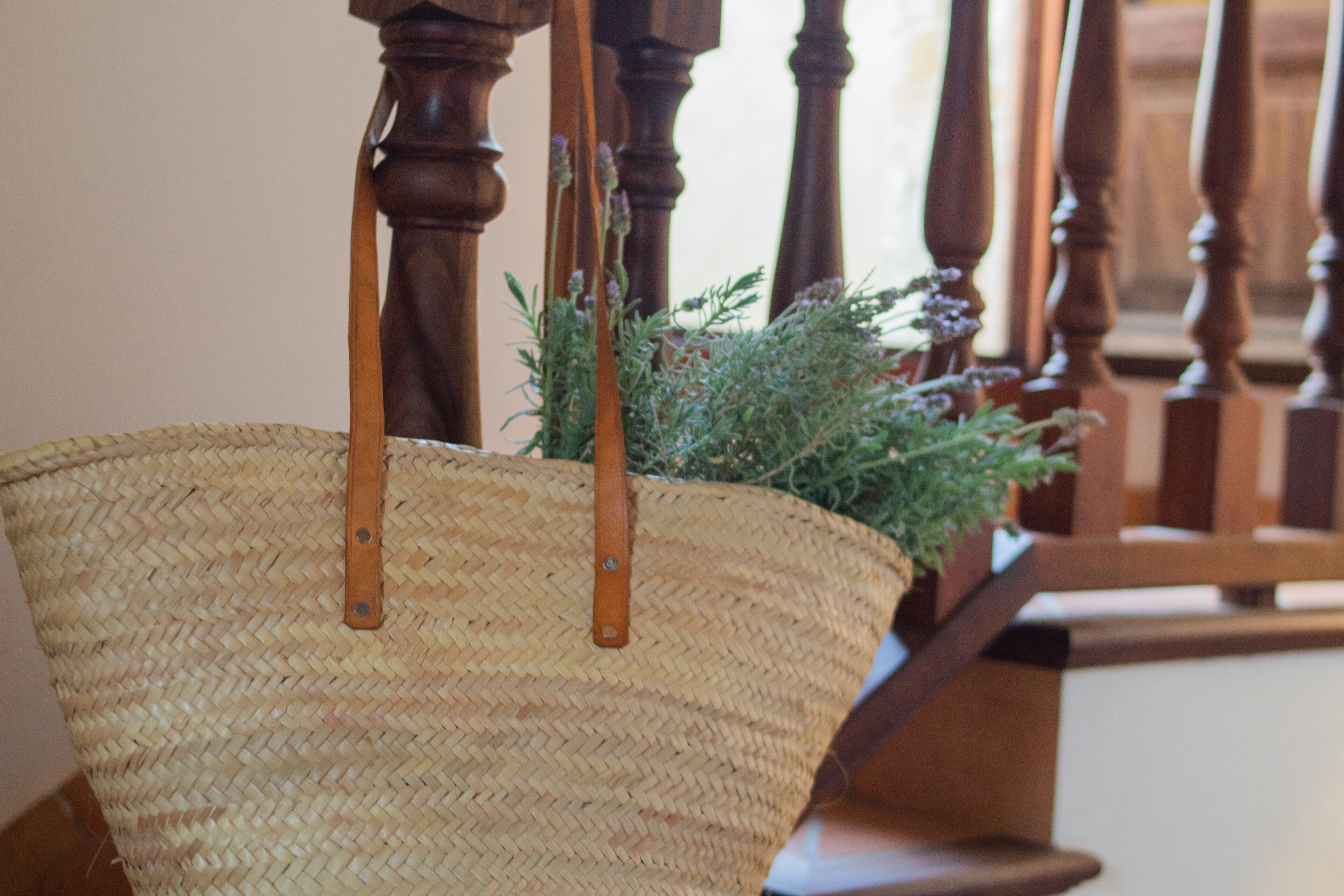 Una cesta tejida con asas, sobre un sillón de madera con asiento tejido.